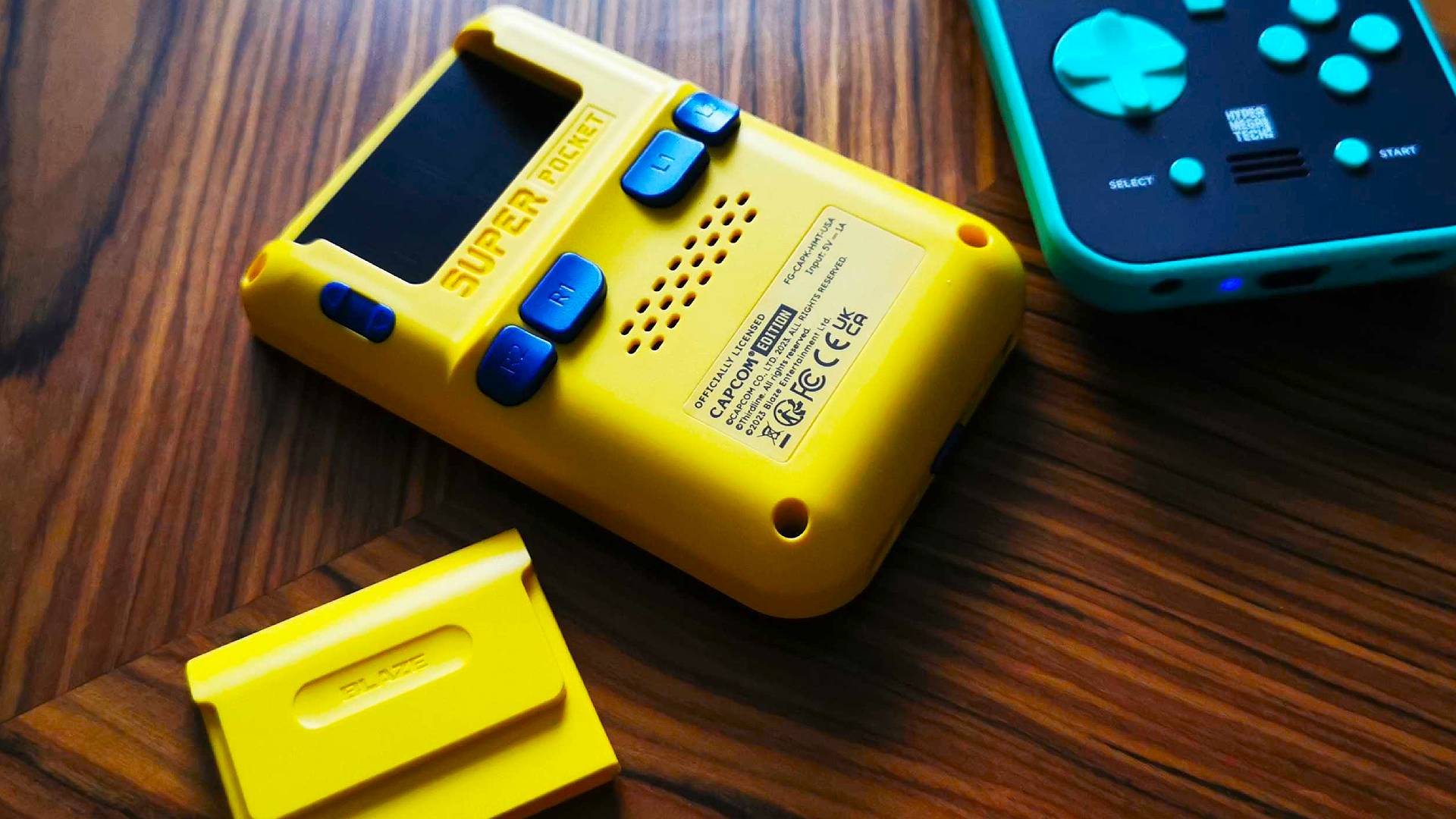 Πίσω όψη του Capcom Super Pocket Handheld στο Woodgrain Table